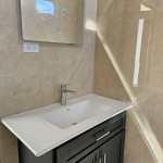 Modern bathroom vanity with a white sink, dark cabinetry, and a mirror on the wall.